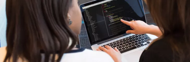 two women looking at code on a computer
